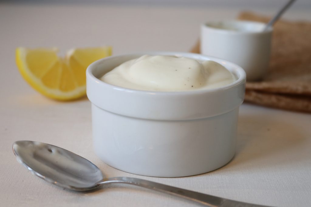 vegane Mayonnaise in einer Schale. Dahinter ein Zitronenschnitz.