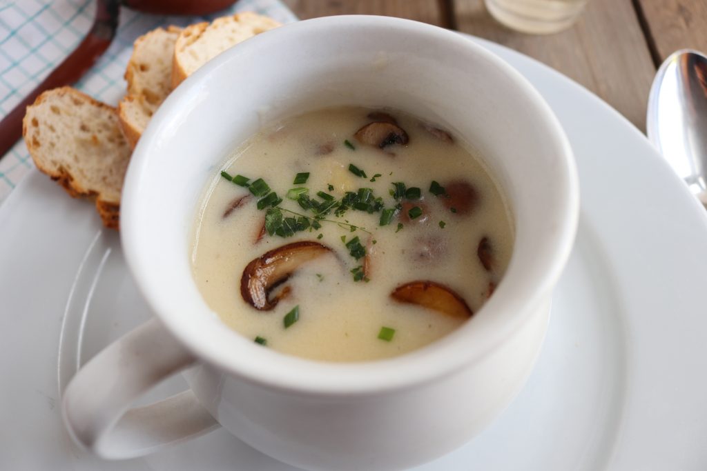 Spargel-Pilz-Cremesuppe in einer Suppentasse auf einem weißen Teller.