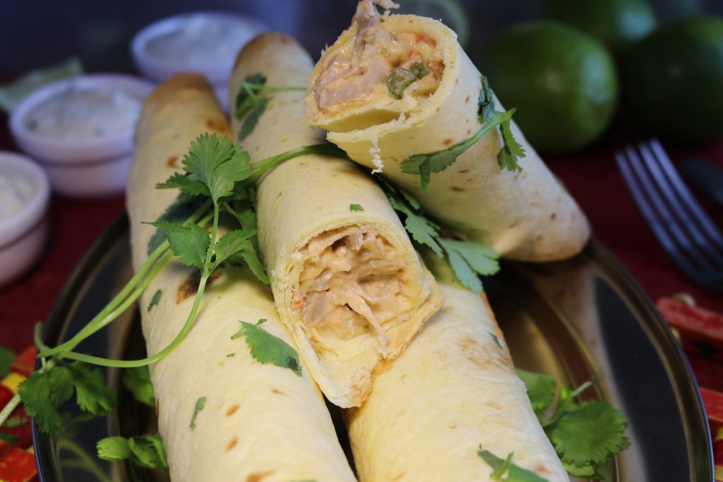 Vegane Chicken Taquitos mit Sour Cream Dip. Ein Taquitos ist angeschnitten, so dass man die Füllung gut sieht.