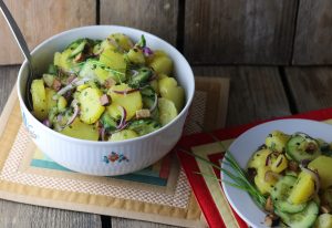 Bayrischer Kartoffelsalat mit Gurke und veganem Speck in einer Schüssel und auf einem Teller.