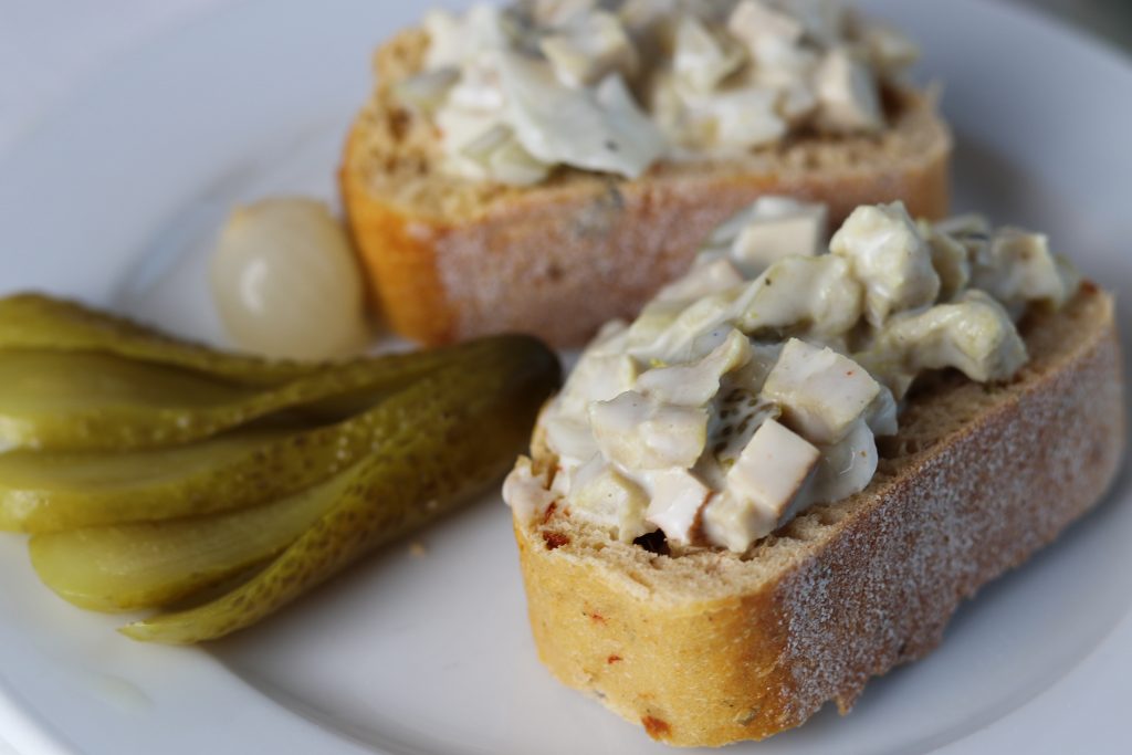 Vleischsalat auf zwei Baguettescheiben, dazu saure Gurke und Silberzwiebeln