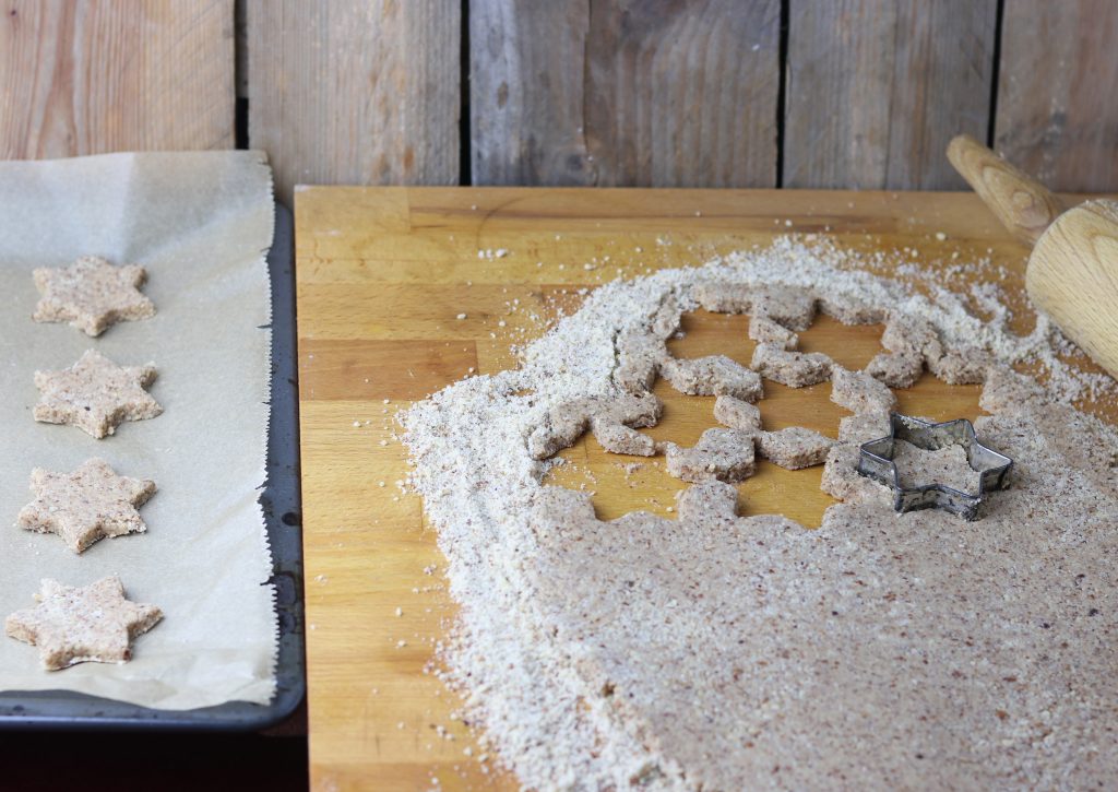 4. Der Zimtsternteig wird auf gemahlenen Haselnüssen ausgerollt und die Plätzchen werden ausgestochen.
