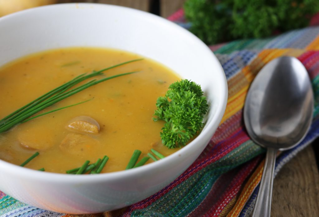 Kartoffelsuppe in einer Schale auf einem bunten Tuch, daneben ein Löffel.