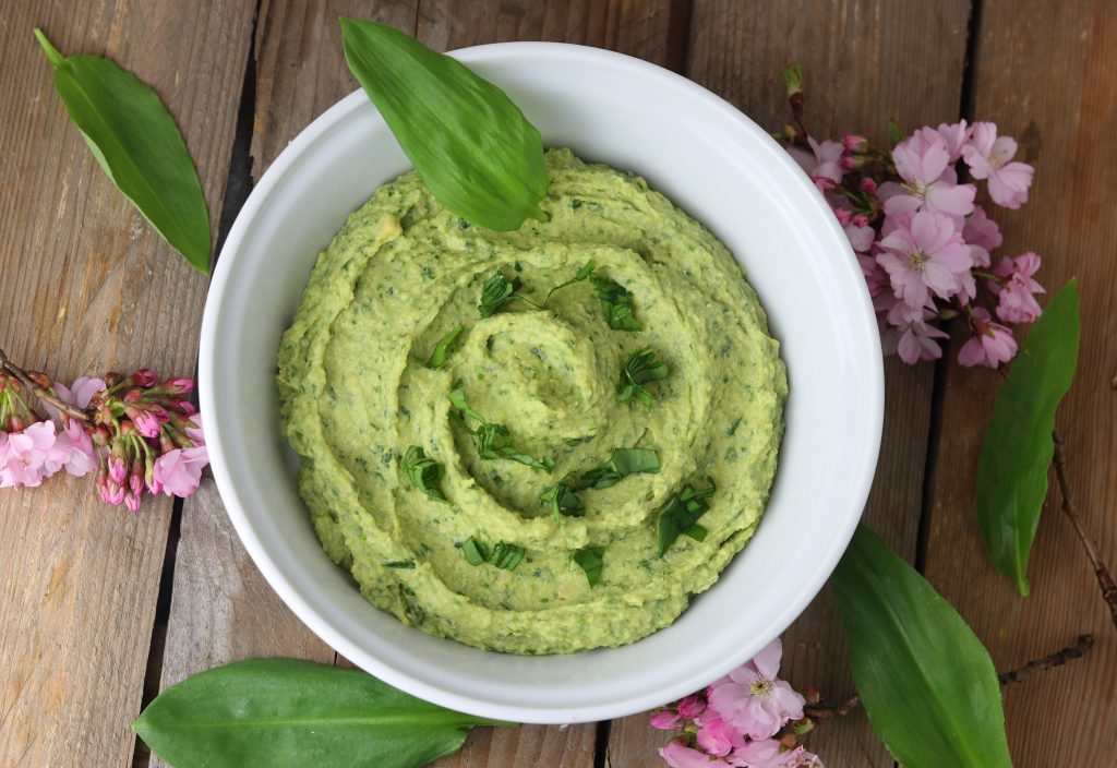 Bärlauchhummus in einer Schale. Drumrum rosa Kirschblüten.