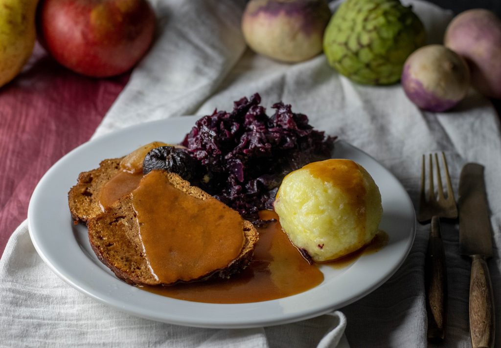Seitanbraten mit Apfelrotkohl, Bratensauce und Knödeln als Beilagen.