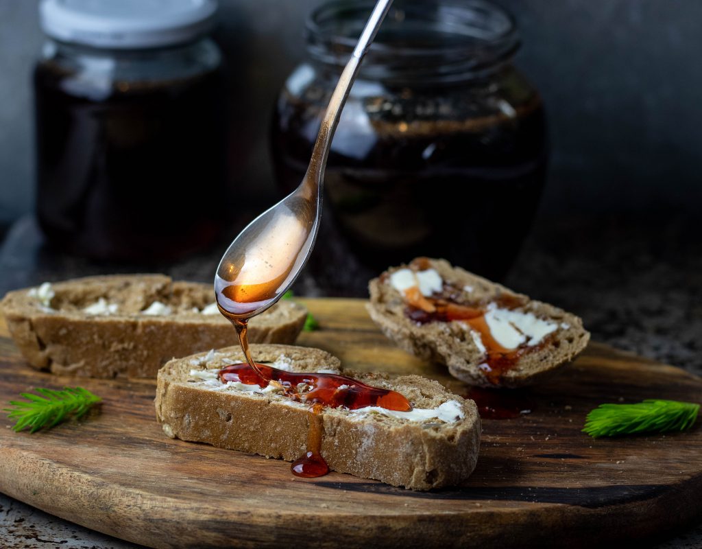 So lecker auf Brot! Ganz leicht kann man aus den jungen Fichtenspitzen, auch Fichtentriebe, Maiwipfeln oder Fichtenwipfeln genannt, einen köstlichen veganen Waldhonig, einen Fichtenspitzenhonig, herstellen.