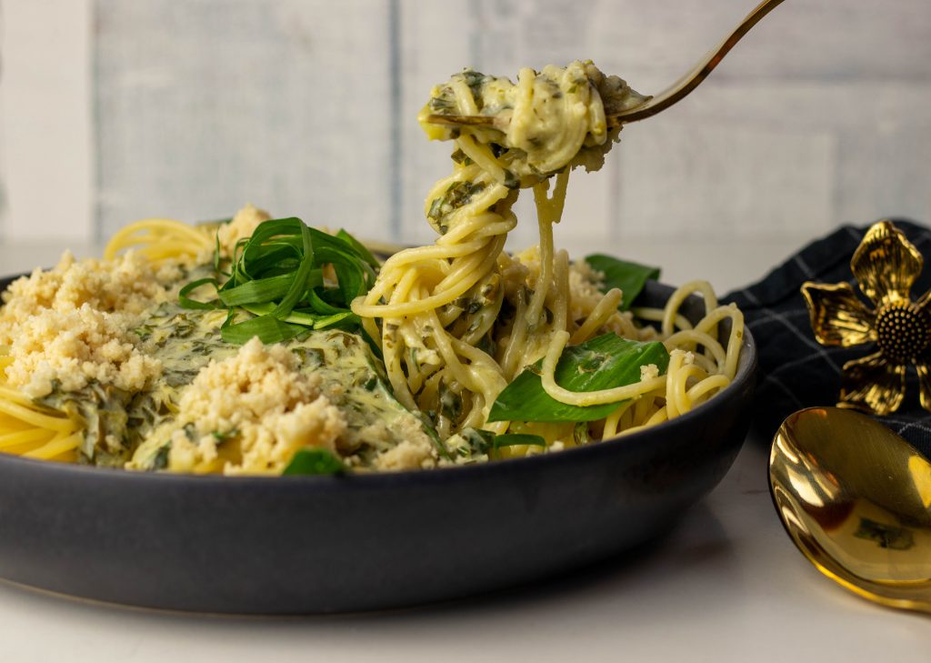Spaghetti mit Limetten-Bärlauchsauce auf einem Teller. Eine goldene Galbel nimmt welche auf.