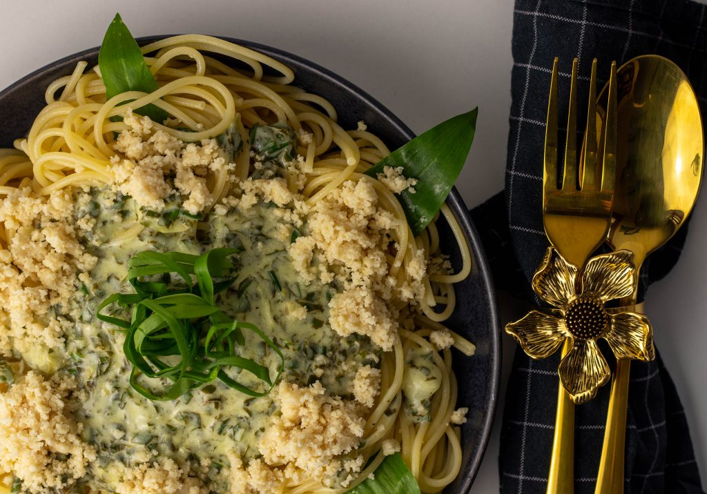 Wunderbare Frühlingsspaghetti: Limetten Bärlauch Spaghetti uf einem schwarzen Teller, daneben goldenes Besteck.