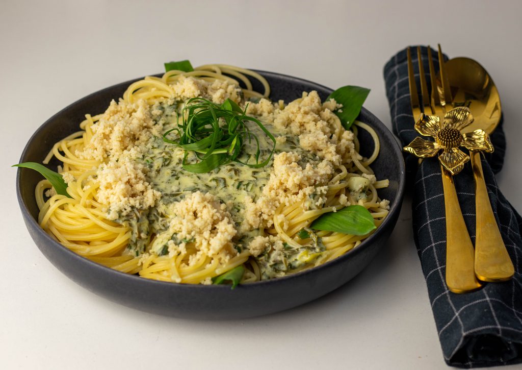 Selbstgemachter, veganer Parmesan auf einem Teller mit Limetten Bärlauch Spaghetti.