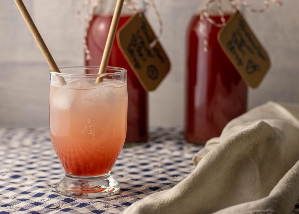 Rhabarber-Ingwer-Bitter-Sirup, als Limo in einem Glas, dahinter zwei Flaschen Sirup