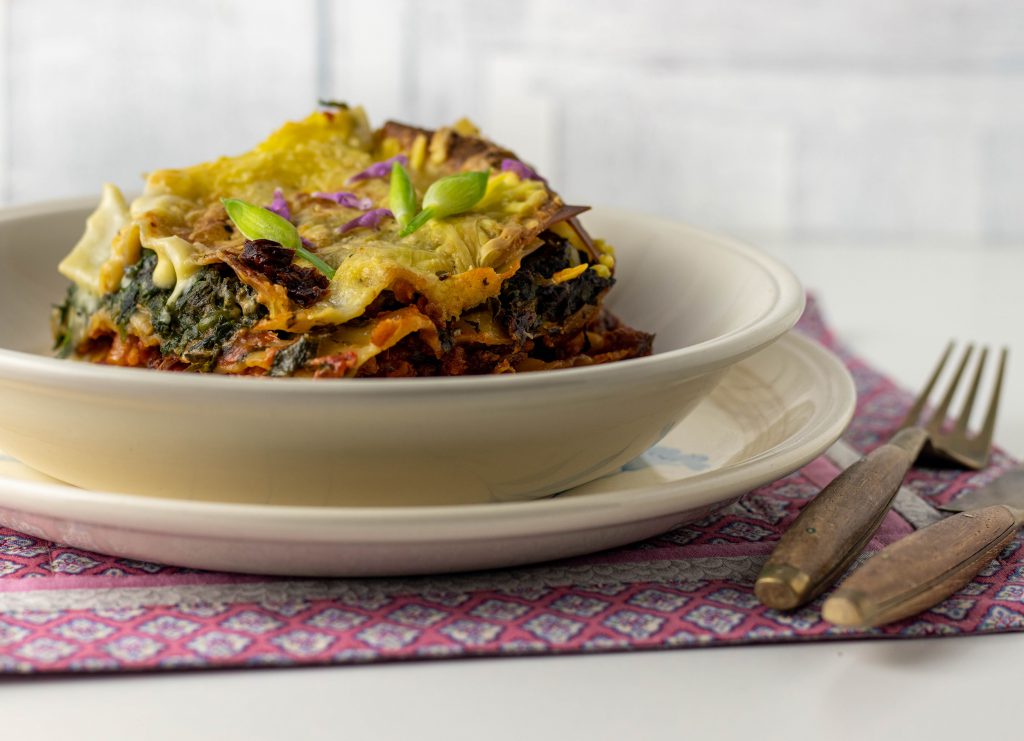 Wildkräuterlasagne. Mit Brennnessel, Bärlauch und Knoblauchsrauke. Auf einem Teller, daneben Besteck.