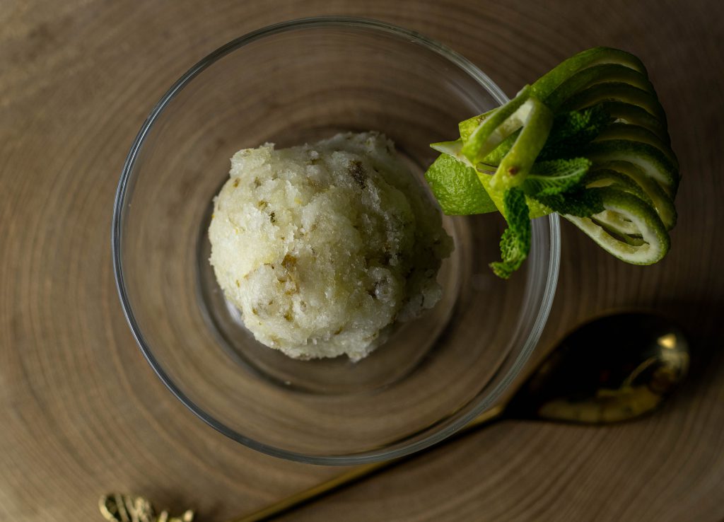 Eine Kugel Limetten-Minz-Sorbet in einem Glasbecher. Mit frischem Minz- und Limettendekor am Rand.