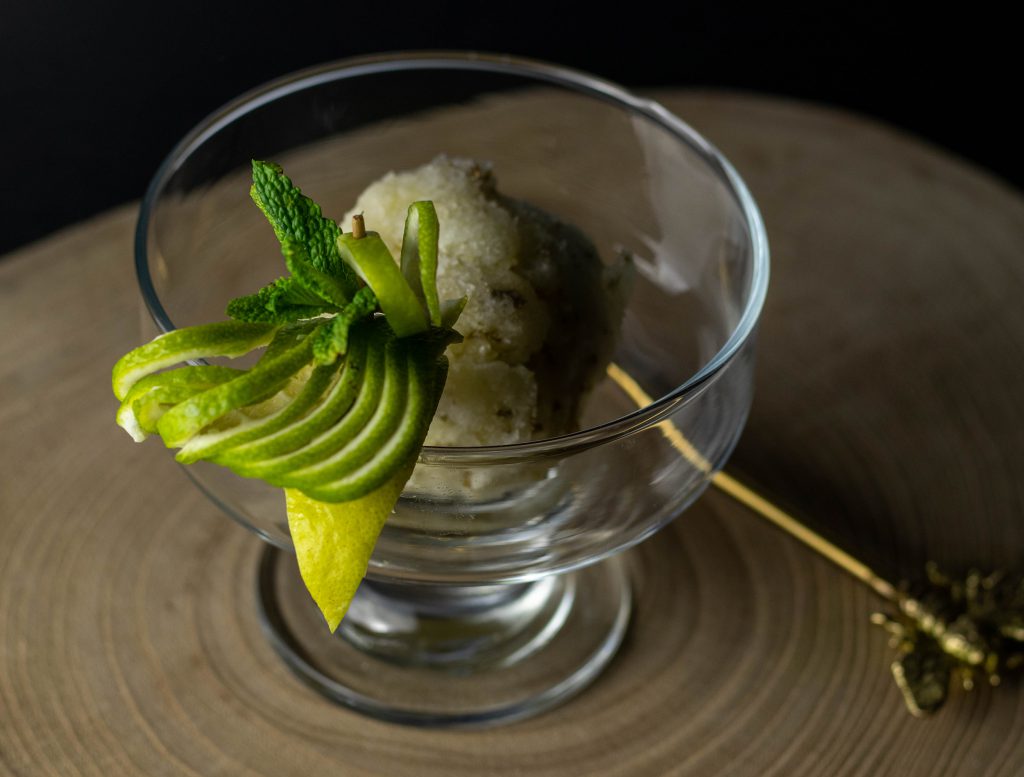 Eine Kugel Limetten-Minz-Sorbet in einem Glasbecher. Mit frischem Minz- und Limettendekor am Rand.
