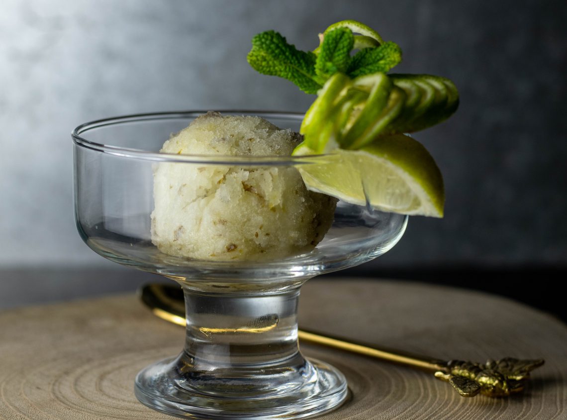 Eine Kugel Limetten-Minz-Sorbet in einem Glasbecher. Mit frischem Minz- und Limettendekor am Rand.