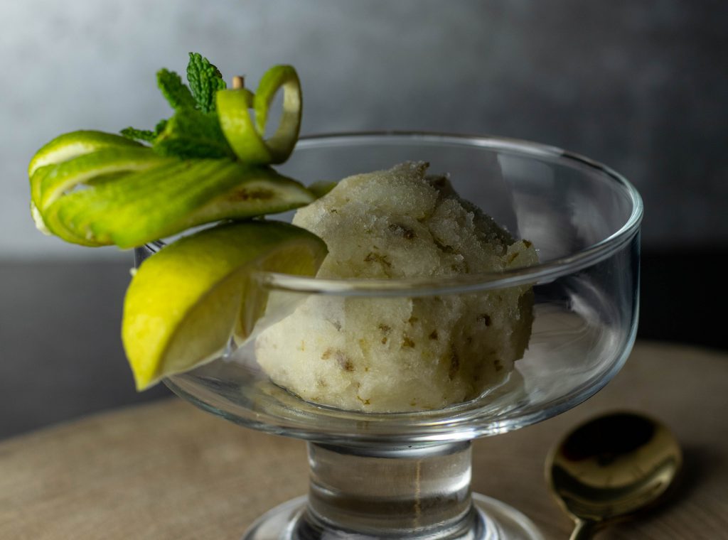 Eine Kugel Limetten-Minz-Sorbet in einem Glasbecher. Mit frischem Minz- und Limettendekor am Rand.