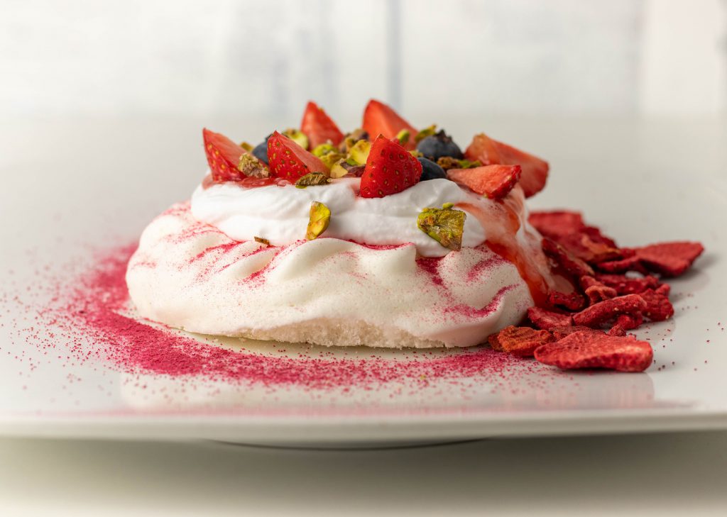 Erdbeer-Pavlova. Knusprig-zarte, vegane Baiserschalen, gefüllt mit Sahne, Erdbeerkompott, frischen Erdbeeren, Blaubeeren, getrockneten Erdbeeren und karamellisierten Pistazien.