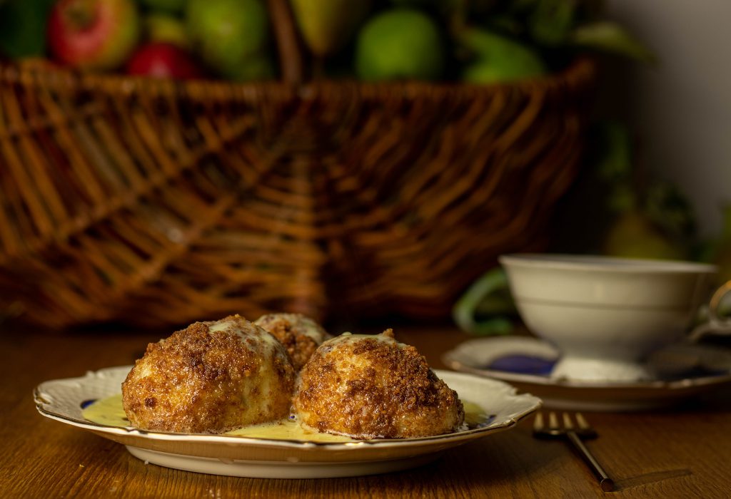 Vegane Zwetschgenknödel im samtigen Quark-Kartoffelteig, gewendet und umhüllt in zimtiger, knuspriger Bröselbutter. Serviert auf süßer Vanille-Tonka-Sauce. 