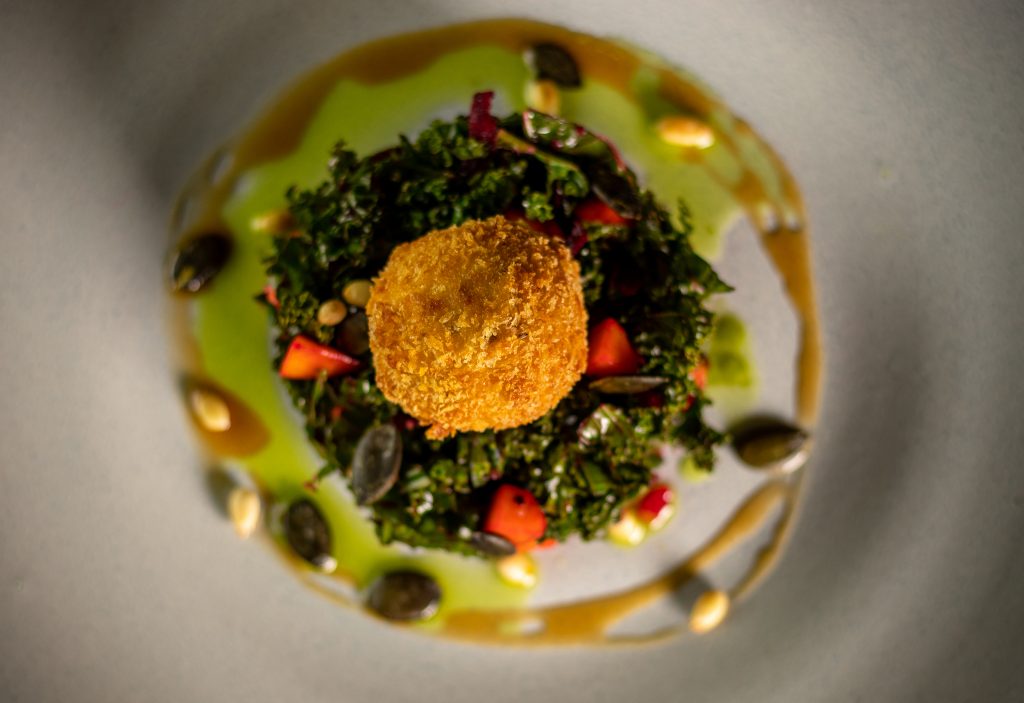 Serviervorschlag: vegane, frittierte, panierte Mozzarellabällchen auf knackigem Grünkohlsalat mit erlesenen Ölen und Crema