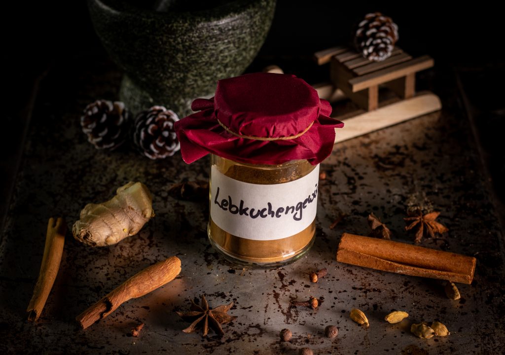 Lebenkuchengewürz auf einem weihnachtlichen Tisch mit Gewürzen und Tannenzapfen.
