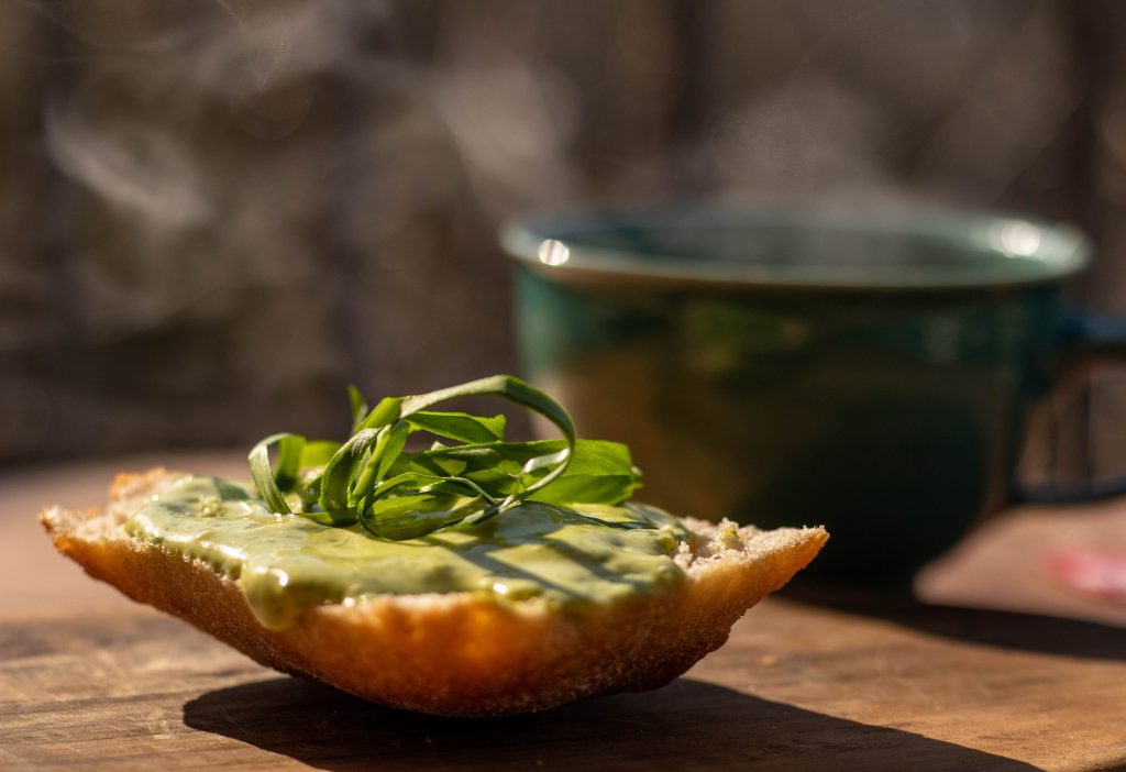 Bärlaquch Aioli auf Brötchen in der Sonne, dahinter eine dampfende Kaffeetasse