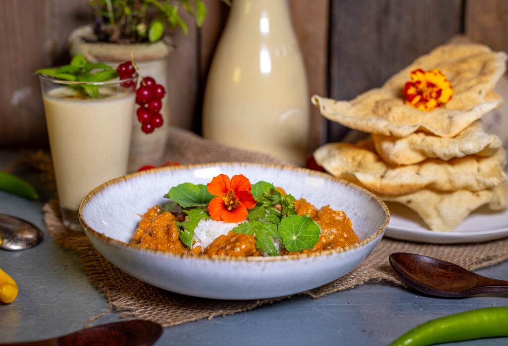 Chicken Makhani, indisches Butterhuhn, hier mit Reis und Papadam als Beilagen. Als Getränk gibt es selbstgemachten Mango-Lassi.