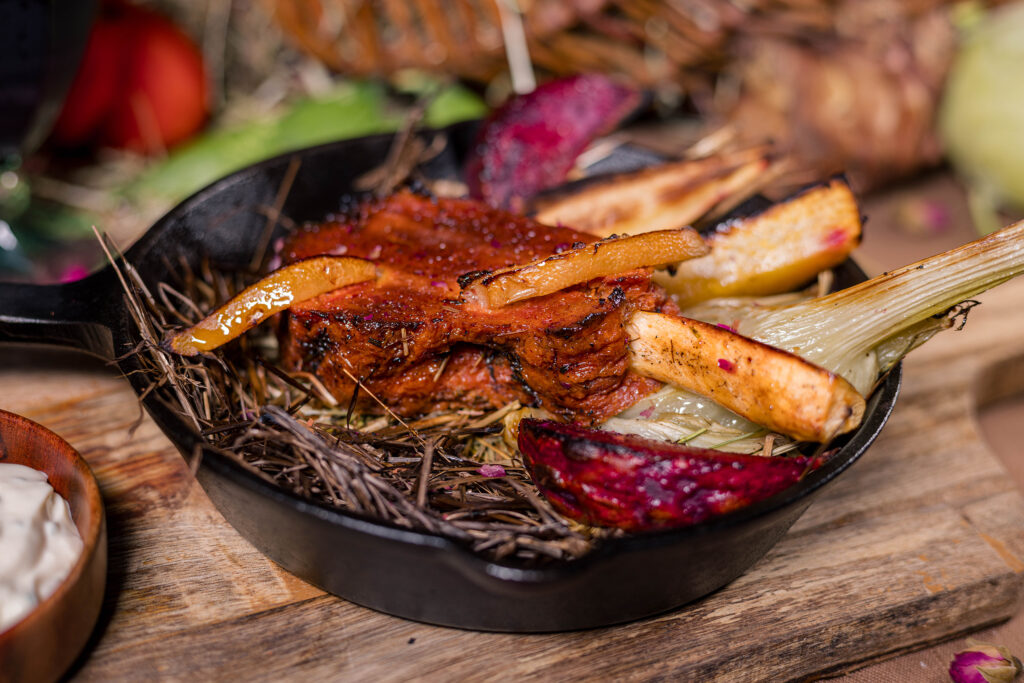 Veganes Seitankarree als Heubraten serviert auf Heu mit Ofengemüse, Salzzitronen und Kräuterquark.
