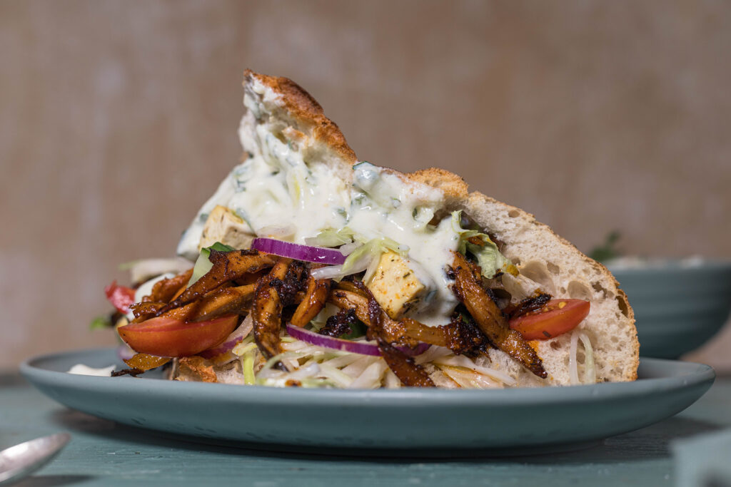 Veganes Gyros im knusprigen Fladenbrot mit veganem Veta, Krautsalat, Tzatziki, sowie Tomaten, Gurke, roter Zwiebel und Tomaten.