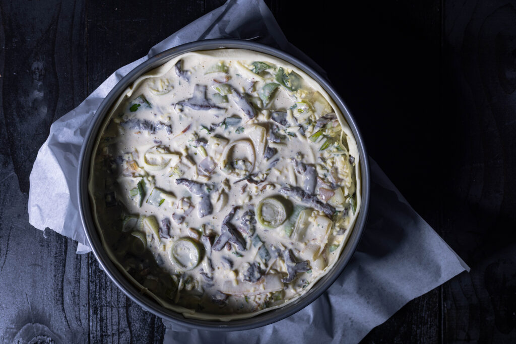 6. Der Pfanneninhalt muss etwas abkühlen und wird dann mit der Creme verührt. Dann kann die Füllung in die Quicheform. Anschließend kommt die Lauch-Pilz-Quiche mit Violetten Rötelritterlingen in den Ofen.