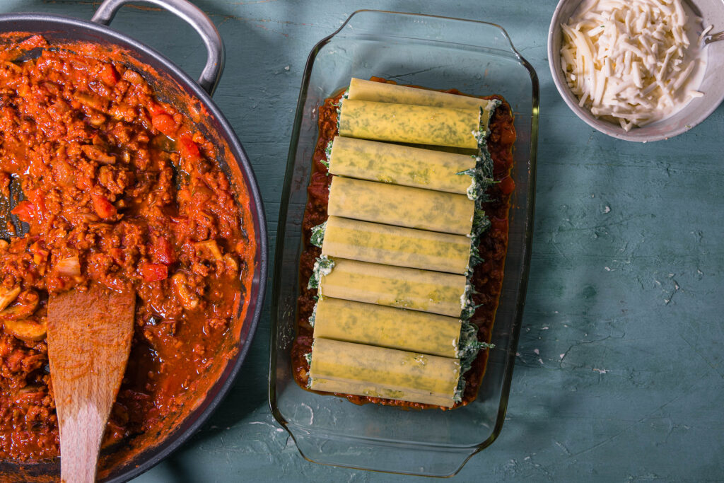 6. Die rohen, gefüllten Cannelloni werden auf einem dünnen Bett aus Bolognese in einer Auflaufform ausgelegt.