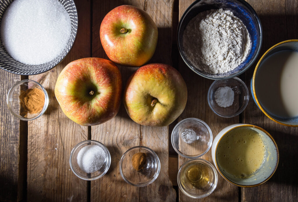 Alle Zutaten für den veganen Apfelküchle auf einem vintage Holztisch.