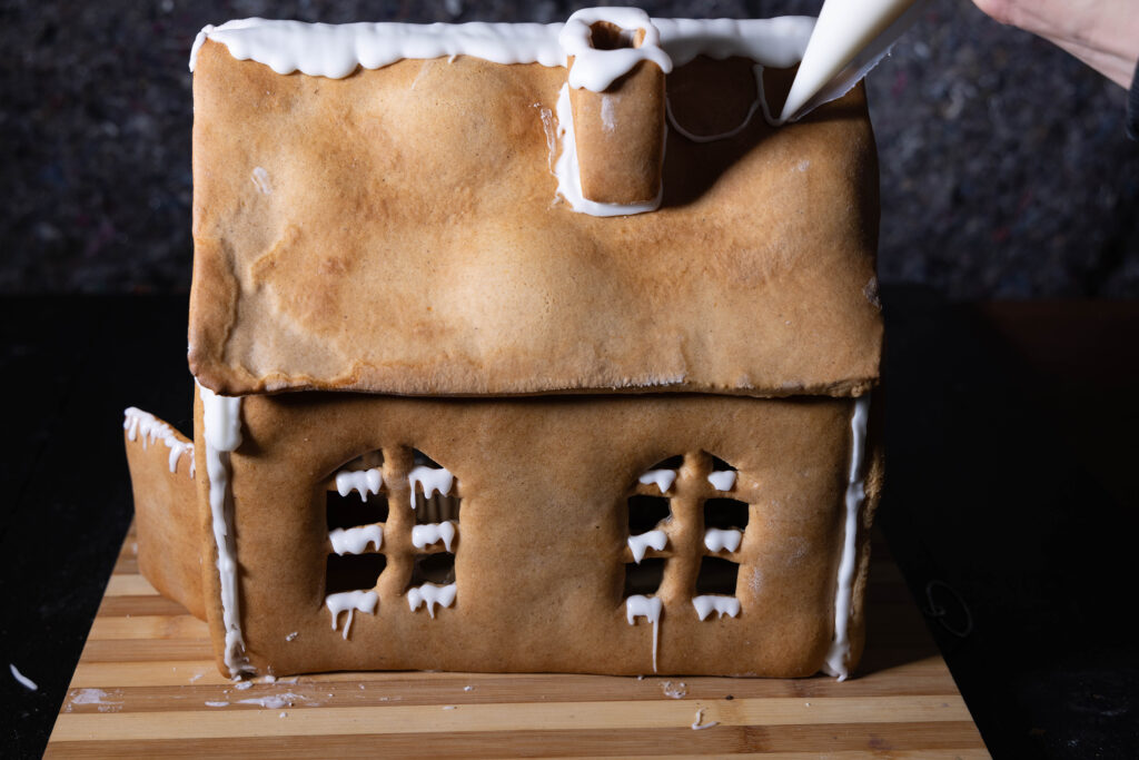 11. Mit dem restlichen Zuckerguss verziere ich das Lebkuchenhaus. Außerdem nehme ich ihn als Kleber, um Süßigkeiten daran zu befestigen.