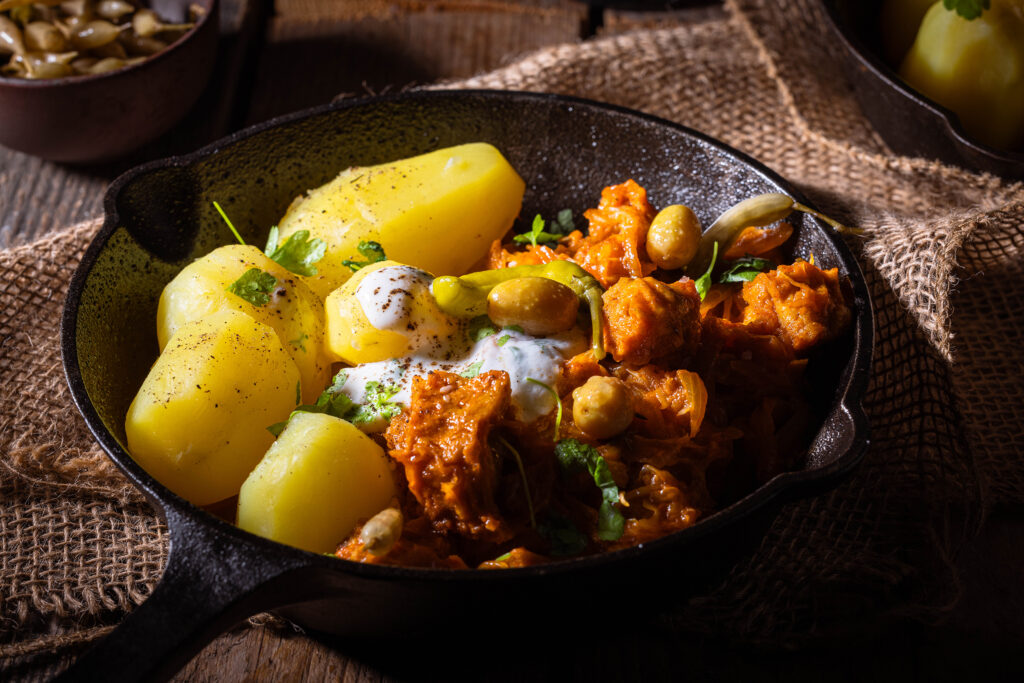 Veganes Szegediner Gulasch mit Kartoffeln, Dip und Petersilie in einer kleinen gußeisernen Pfanne