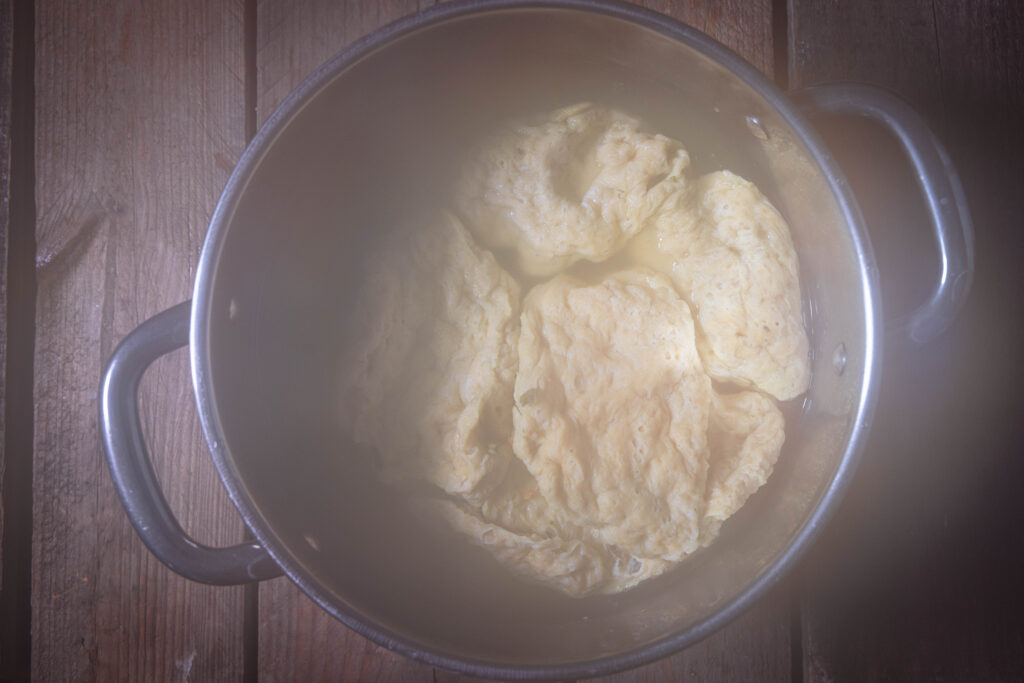 Ein dampfender Topf von oben mit Seitanscheiben, die in Brühe kochen, darin.