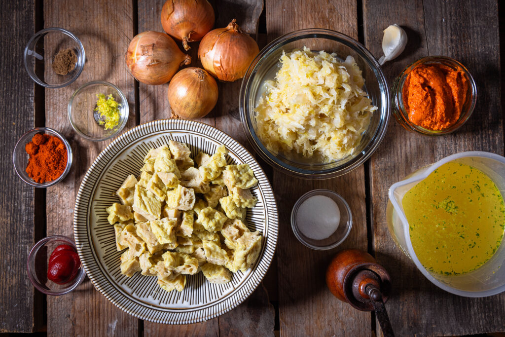 Alle Zutaten für das vegane Szegediner Gulasch auf einem Holztisch.
