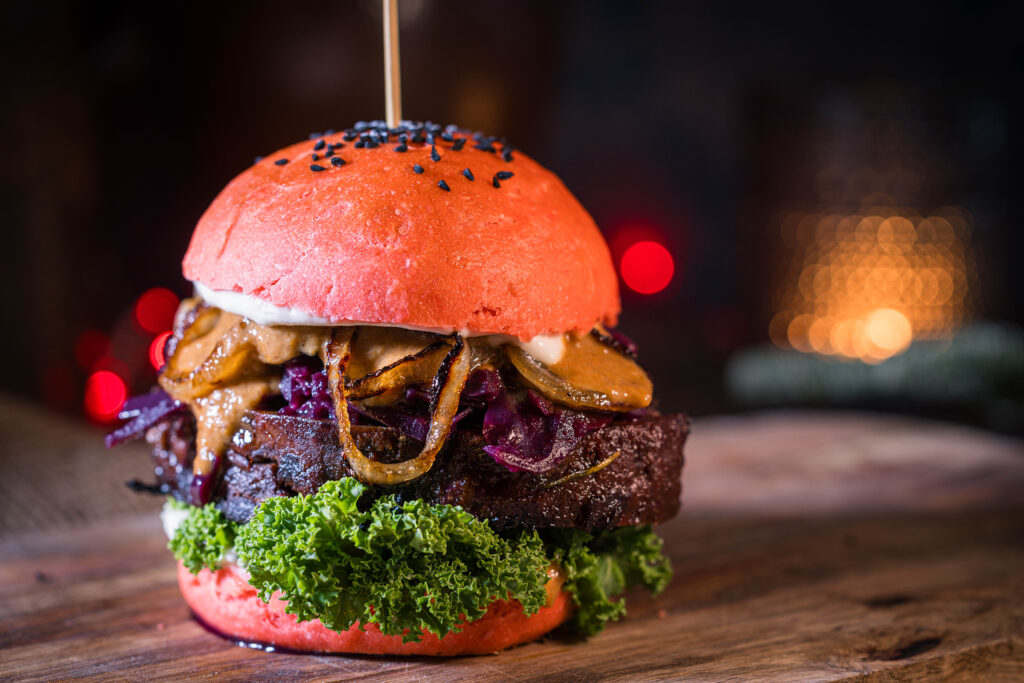 Weihnachtsburger auf Holzbrett, dahinter verschwommen eine brennende Kerze und rote Lichter