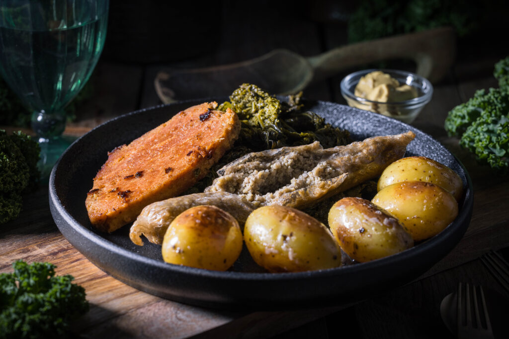 Bremer Grünkohl vegan – mit selbstgemachter Pinkel und Kasseler - angerichtet auf einem schwarzen Teller. Daneben eine Schale Senf.