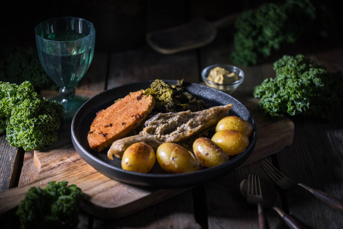 Bremer Grünkohl mit Pinkel und Kassler, vegan. Auf einem dunklen Teller auf einem Holztisch