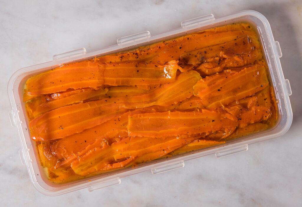 Eine längliche Plastikdose mit langen Karottenstreifen darin, in einer Marinade.