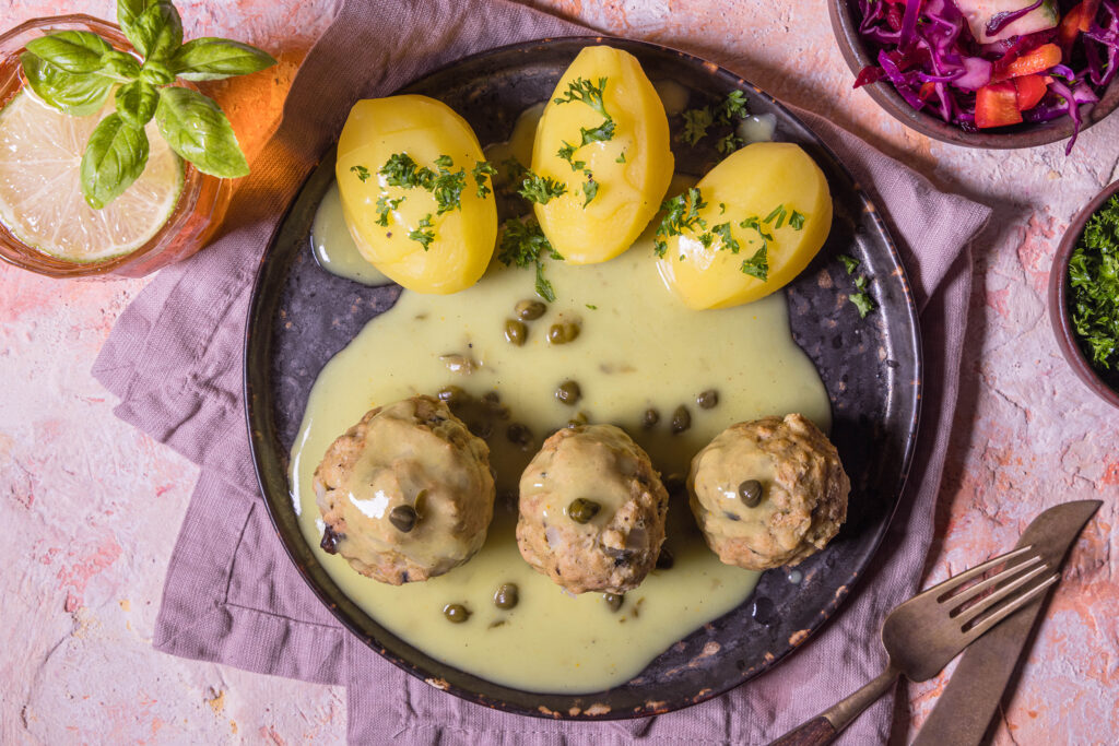 3 Königsberger Klopse – rein pflanzlich und selbstgemacht - mit Kartoffeln und Kapernsauce auf einem Teller.