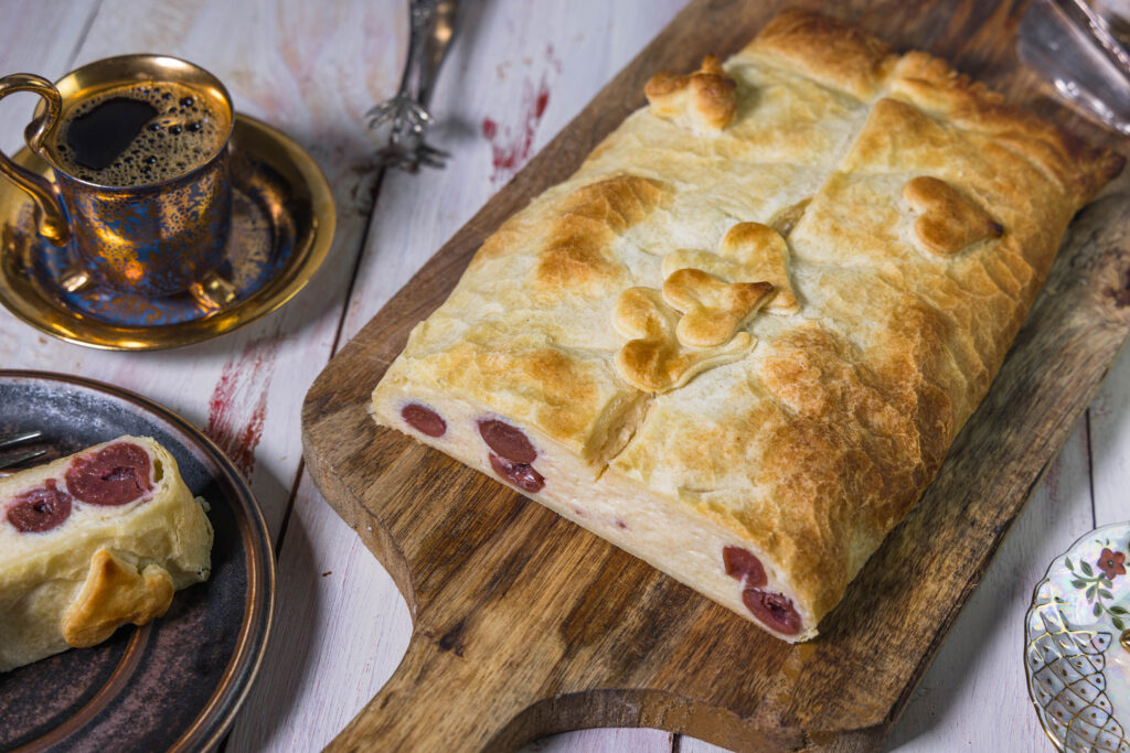 Angeschnittener Quarkstrudel mit Kirschen auf einem Holzbrett.