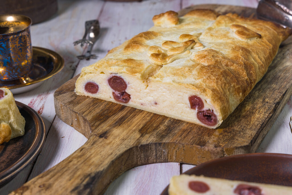 Veganer Quarkstrudel mit Kirschen und Blätterteig im Anschnitt. Man sieht auch die rubinroten Kirschen sehr gut.
