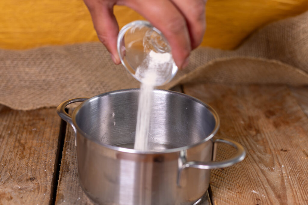 Eine Hand gibt Agar Agar aus einer kleinen Schale in einen Topf.