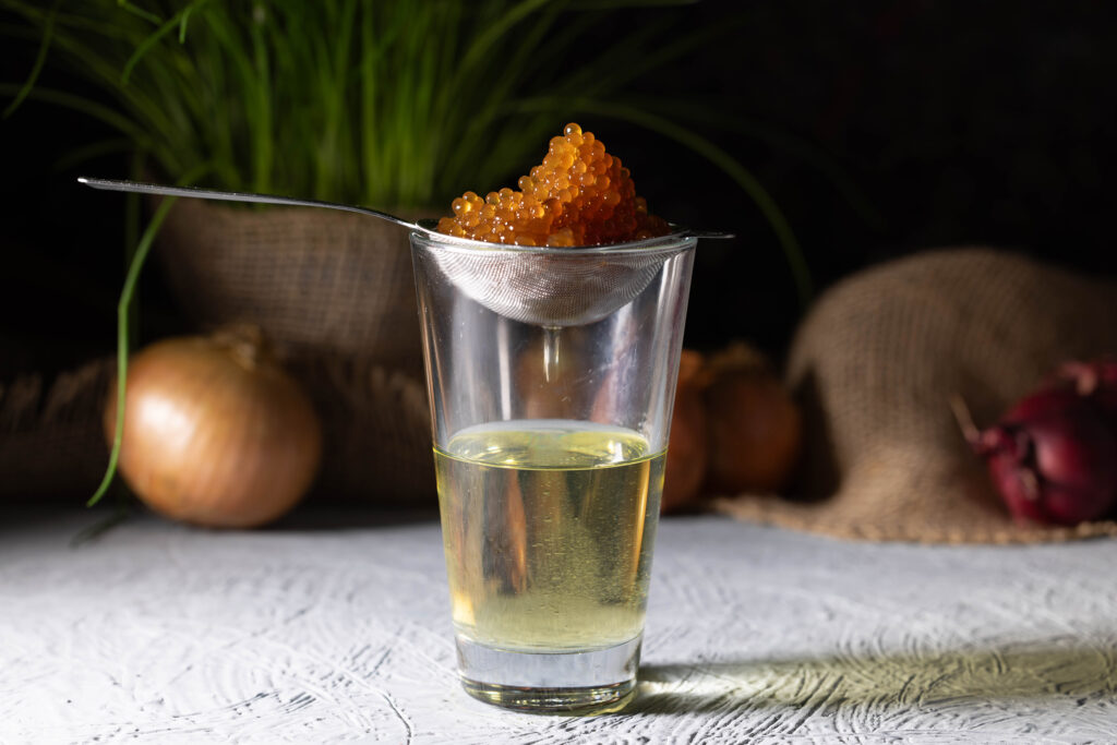 Veganer Kaviar mit dem Aroma karamellsierter Zwiebeln tropft in einem Teesieb über einem Glas ab.