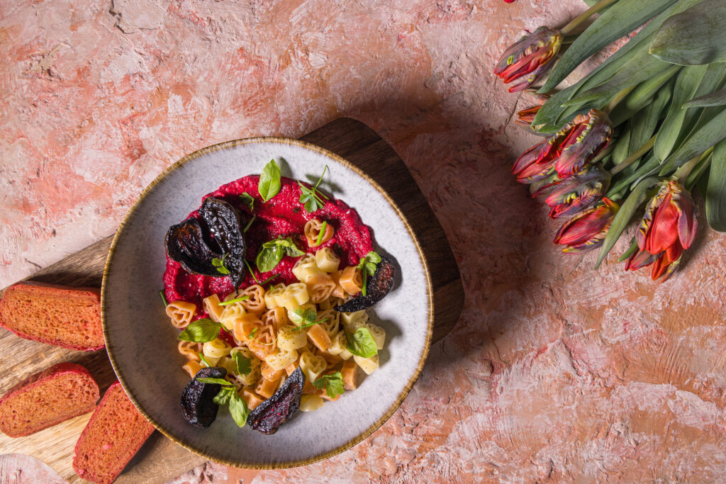 Herzchenförmige Pasta mit Rote Beete Hummus Sauce. Daneben drei Scheiben rosa Pfannenbrot und Tulpen.