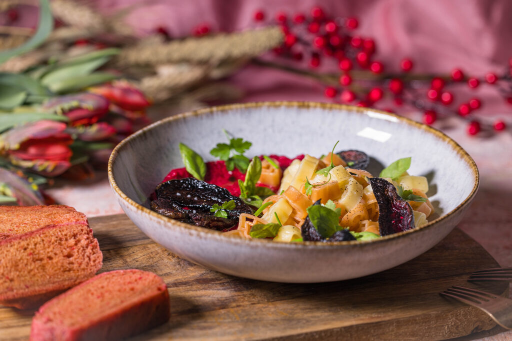 Herzchenförmige Pasta mit Rote Beete Hummus Sauce. Daneben drei Scheiben rosa Pfannenbrot und Tulpen.