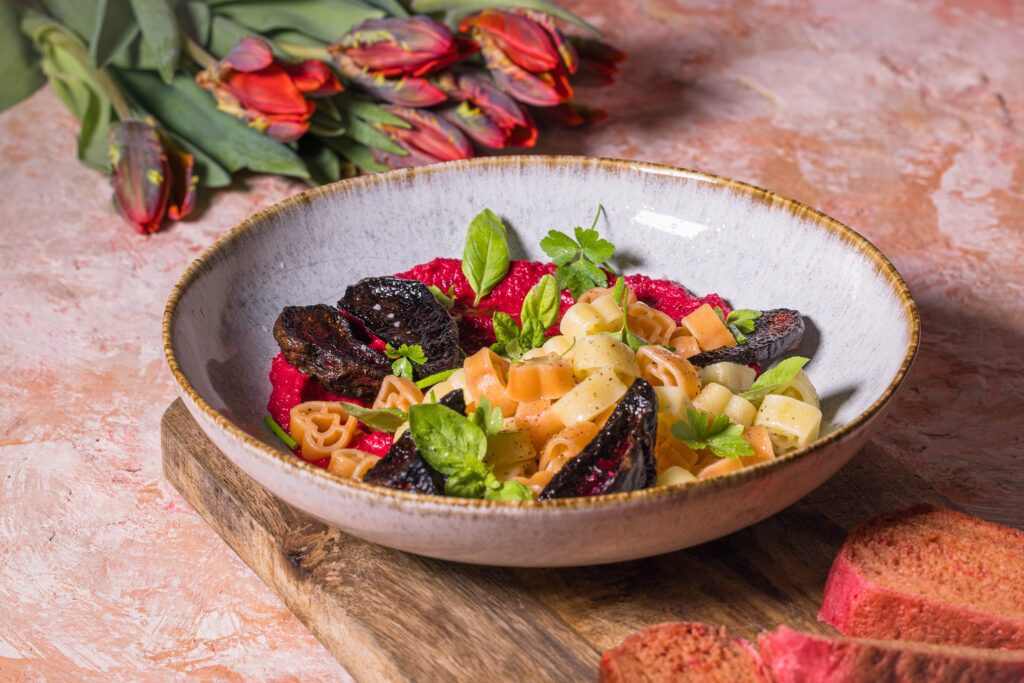 Herzchenförmige Pasta mit Rote Beete Hummus Sauce. Daneben drei Scheiben rosa Pfannenbrot und Tulpen.