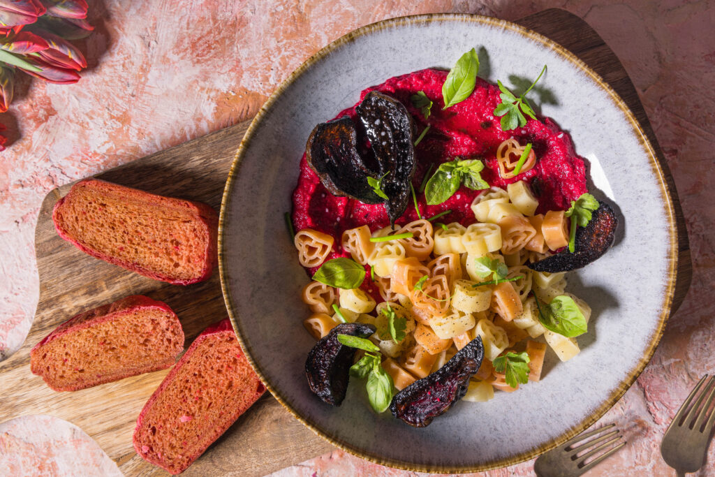 Herzchenförmige Pasta mit Rote Beete Hummus Sauce. Daneben drei Scheiben rosa Pfannenbrot und Tulpen.