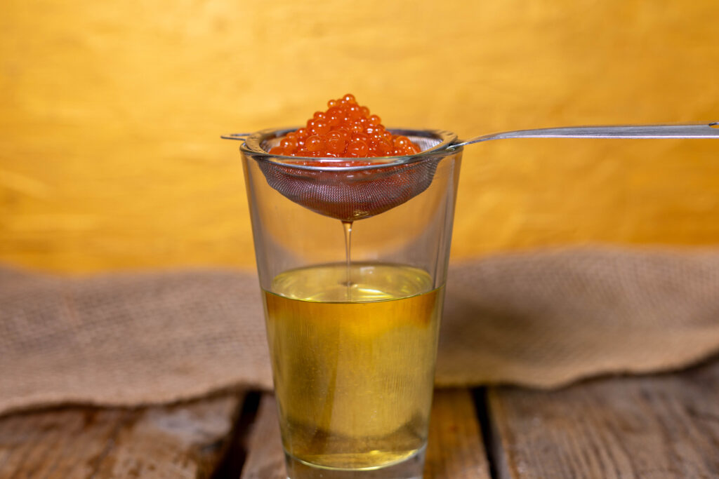 Veganer Kaviar mit Chiligeschmack tropft über einem Glas ab.