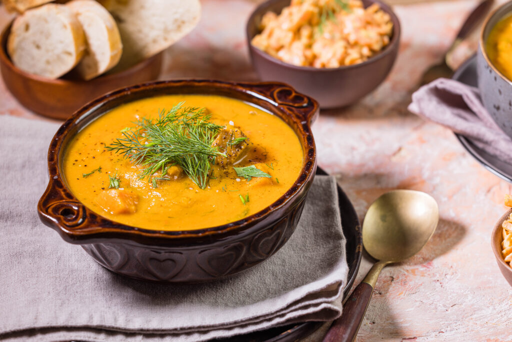 Süßkartoffel-Kokos-Suppe in einer Schüssel mit Karottensalat und Brot als Beilage daneben.