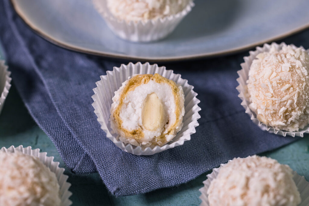 Ein halbierter, veganer, selbstgemachter Raffaello, Vaffaello. Man sieht die Waffel mit der Kokoshülle außen und die Kokoscreme, sowie die Mandel innen.